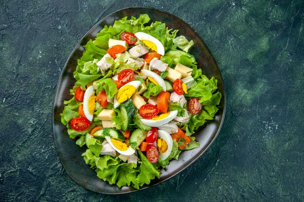 Draufsicht des hausgemachten köstlichen Salats in einer schwarzen Platte auf grünem schwarzem Mischfarbenhintergrund mit freiem Raum