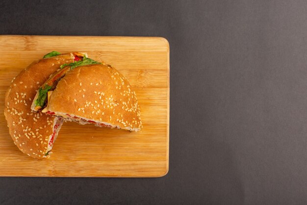 Draufsicht des Hühnchensandwiches mit grünem Salat und Gemüse innerhalb der Hälfte, die auf Holzoberfläche geschnitten wird