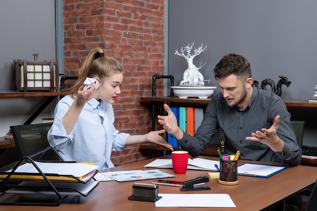 Draufsicht des jungen lustigen Büroteams, das bei einem Problem in der Büroumgebung verwirrt ist