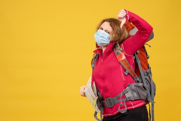 Draufsicht des jungen reisenden Mädchens in der medizinischen Maske, die ihr Gepäck sammelt und schlechte Geste macht