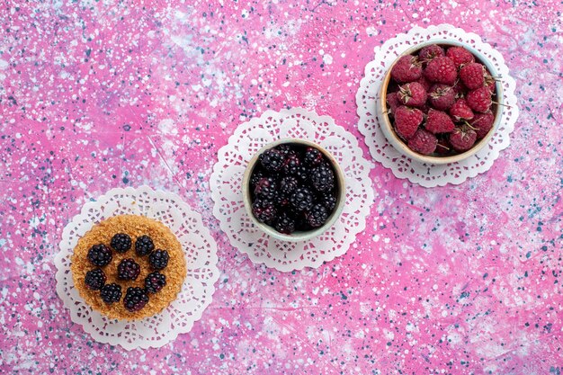 Draufsicht des kleinen Brombeerkuchens mit Himbeeren und frischen Brombeeren auf der hellrosa Oberfläche