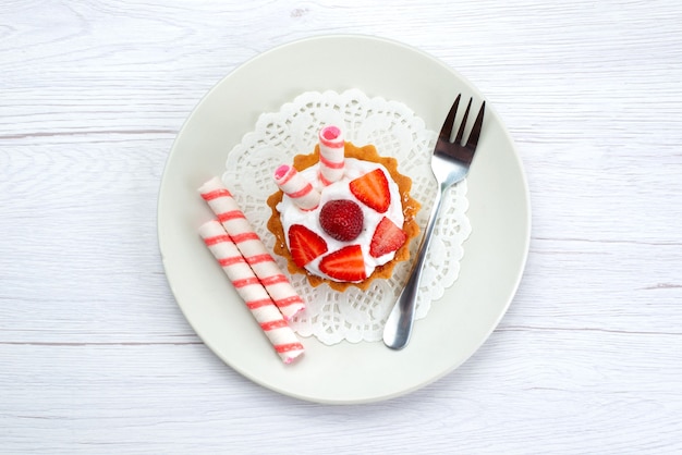 Draufsicht des kleinen Kuchens mit Sahne und geschnittenen Erdbeeren innerhalb der Platte auf weißem süßem Zucker der Obstkuchenbeere