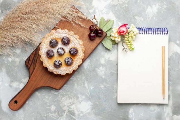 Draufsicht des kleinen Kuchens mit Zuckerpulverfruchtcreme und -block auf leichtem süßem Tee der Kuchencremefrucht