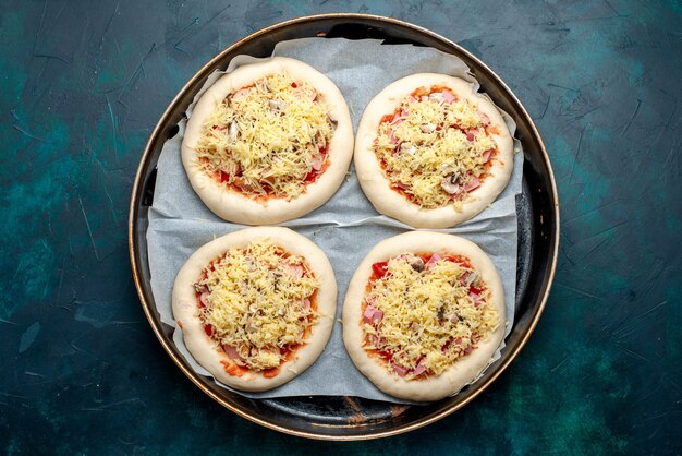 Draufsicht des kleinen rohen Pizzateigs mit Gemüse und Käse innerhalb der Pfanne auf der dunkelblauen Oberfläche