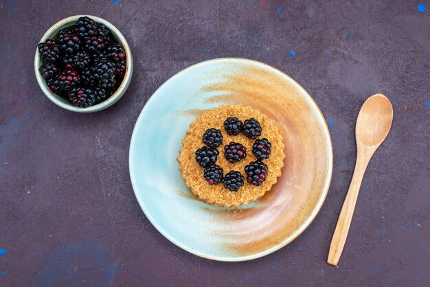 Draufsicht des kleinen runden Kuchens mit Beeren innerhalb Platte auf dunkler Oberfläche