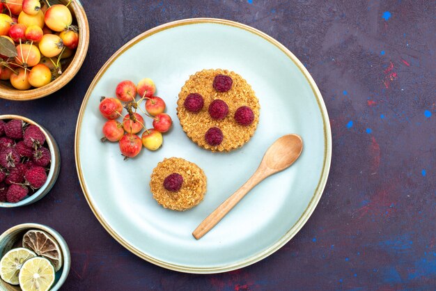 Draufsicht des kleinen runden Kuchens mit frischen Himbeeren innerhalb Platte mit Früchten auf der dunklen Oberfläche