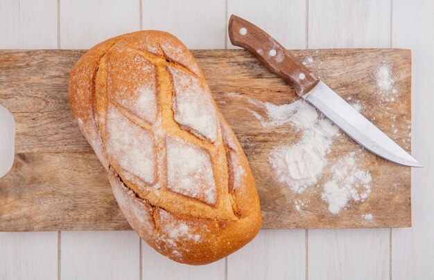 Draufsicht des knusprigen Brotes mit Messer und Mehl auf Schneidebrett auf hölzernem Hintergrund
