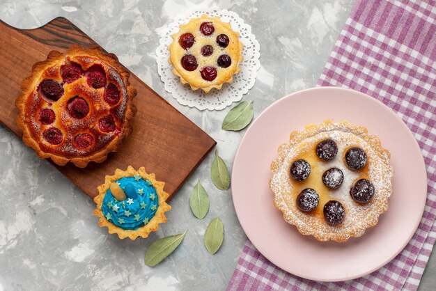 Draufsicht des köstlichen Himbeerkuchens mit kleinen Kuchen auf hellem Schreibtisch, Kuchenfrucht-Beeren-Torte