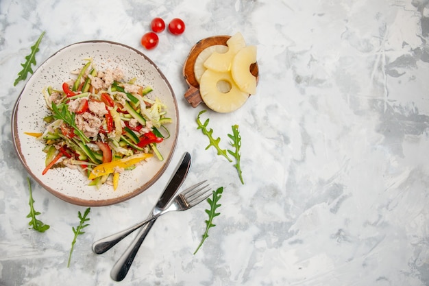 Draufsicht des köstlichen Hühnchensalats mit Gemüsetomaten getrocknetem Ananasbesteck auf der rechten Seite auf befleckter weißer Oberfläche gesetzt