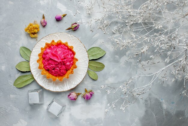 Draufsicht des köstlichen kleinen Kuchens mit rosa Sahne und Pralinen auf leichtem, süßem Sahne-Tee-Auflauf des Kuchens