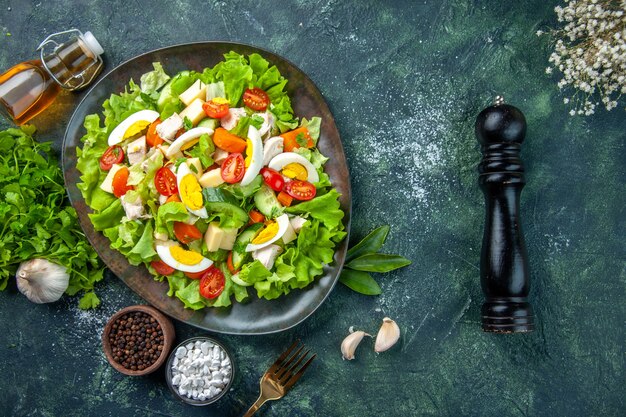 Draufsicht des köstlichen Salats mit vielen frischen Zutatengewürzen Knoblauch gefallene Ölflaschenblume auf schwarzgrünem Mischfarbenhintergrund