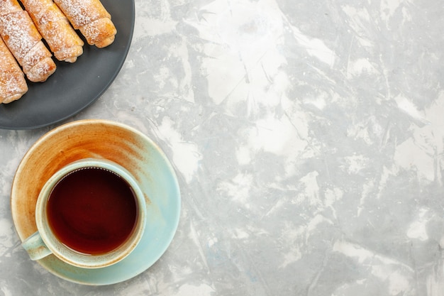 Draufsicht des köstlichen Teigs des Zuckerpulver-Bagels mit Tasse Tee auf weißer Oberfläche