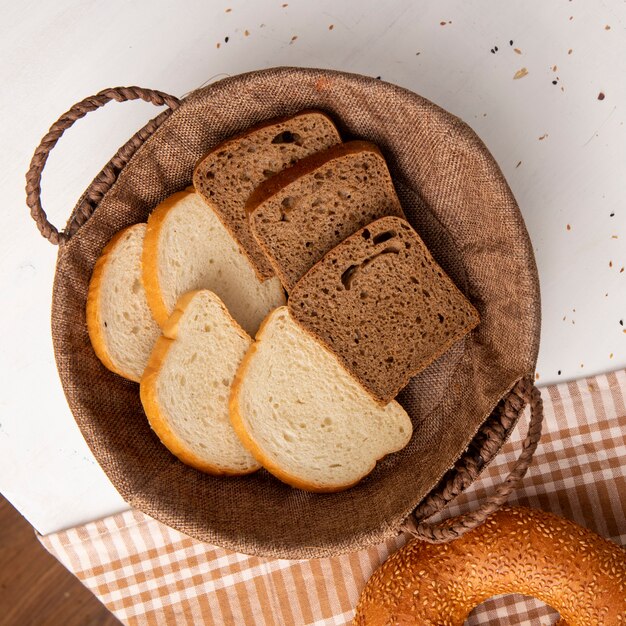 Draufsicht des Korbs voll von Weiß- und Roggenbrotscheiben mit Bagel auf Stoff auf weißem Hintergrund