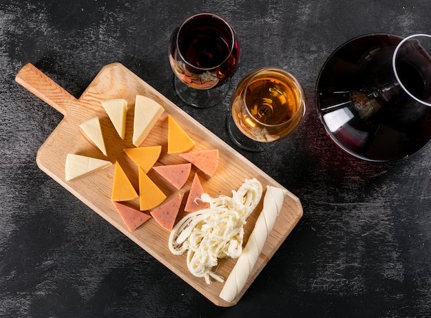 Draufsicht des Kruges mit Wein und Käse auf hölzernem Schneidebrett auf dunkler Horizontaler