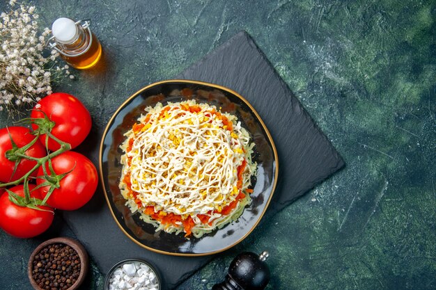 Draufsicht des leckeren Mimosensalats innerhalb der Platte mit roten Tomaten auf dunkelblauer Oberfläche