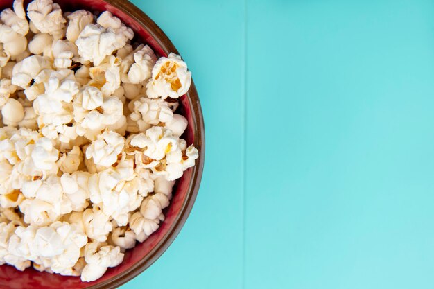 Draufsicht des leckeren Popcorns auf einer Holzschale auf blauer Oberfläche