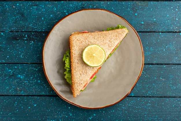 Draufsicht des leckeren Sandwichs mit grünen Salattomaten auf dem blauen Schreibtisch