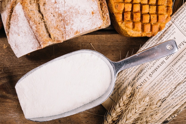 Draufsicht des Mehls in der Schaufel mit gebackenem Brot auf Holztisch