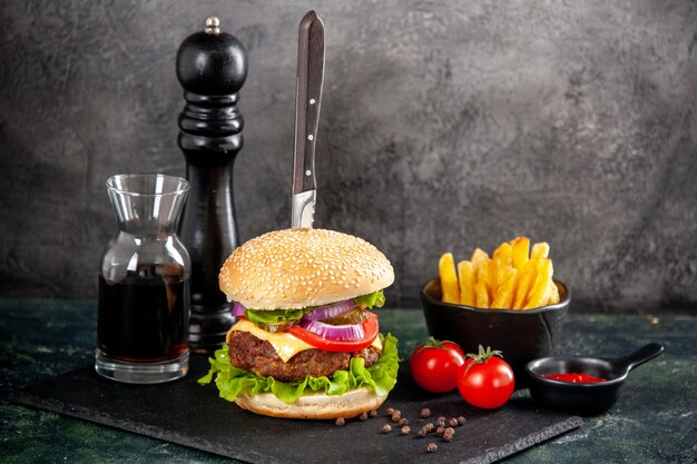 Draufsicht des Messers im köstlichen Fleischsandwich und im grünen Pfeffer auf Ketchup-Tomaten der schwarzen Tablettsauce mit Stielfritten auf dunkler Oberfläche