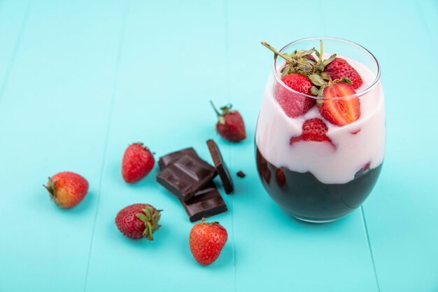 Draufsicht des Milchshakes auf einem Glas mit Schokolade und Erdbeeren mit Schokoriegel auf blauer Oberfläche