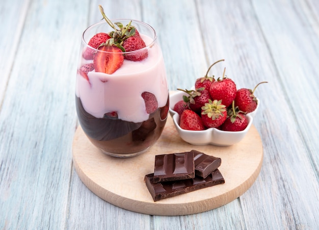 Draufsicht des Milchshakes mit Erdbeeren und Schokolade auf einem hölzernen Küchenbrett auf grauer Oberfläche