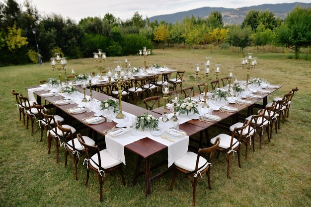 Draufsicht des mit minimalen Blumensträußen dekorierten Hochzeitsfeier-Tisches mit Chiavari-Sitzen draußen in den Gärten mit Blick auf die Berge