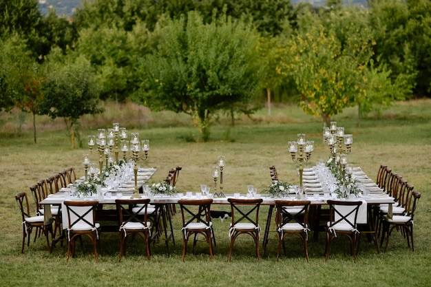 Draufsicht des mit minimalen Blumensträußen und Kerzen dekorierten Hochzeitsfeier-Tisches mit Chiavari-Sitzen draußen in den Gärten vor Obstbäumen