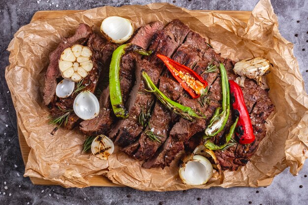 Draufsicht des mittleren gekochten Steaks mit Knoblauch, Zwiebel, rotem und Chili-Pfeffer auf Pergamentpapier