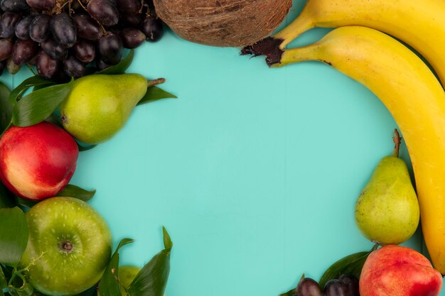 Draufsicht des Musters von Früchten als Kokosnussbirnenpfirsich-Traubenbananenapfel mit Blättern auf blauem Hintergrund mit Kopienraum