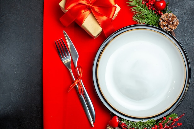 Draufsicht des Neujahrshintergrunds mit Esstischbesteck stellte Dekorationszubehör Tannenzweige neben einem Geschenk auf einer roten Serviette ein