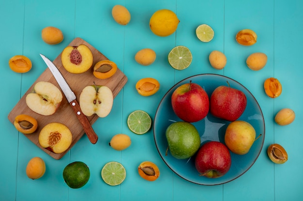 Draufsicht des Pfirsichs mit einem Apfel auf einem Brett mit einem Messer Aprikosen und Limette mit Zitrone auf einer hellblauen Oberfläche