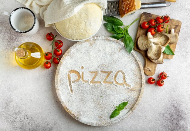Draufsicht des Pizzateigs mit Pilzen und Tomaten und Wort geschrieben in Mehl