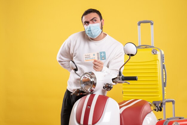 Draufsicht des Reisekonzepts mit neugierigem jungem Mann in medizinischer Maske, der in der Nähe des Motorrads steht