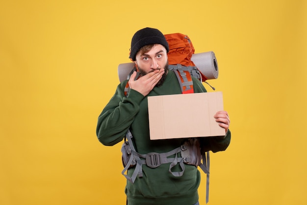 Kostenloses Foto draufsicht des reisekonzepts mit verwirrtem jungen kerl mit packpack, der freien raum zum schreiben hält
