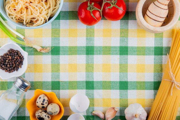 Draufsicht des rohen und gekochten hölzernen mörsers der frischen und gekochten spaghetti-nudeln und der kleinen wachteleier auf tischdecke