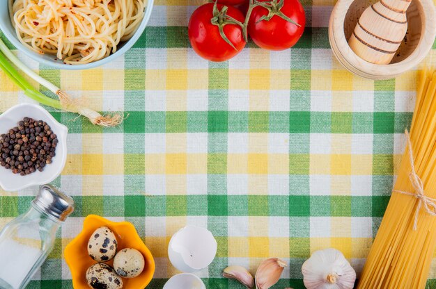 Draufsicht des rohen und gekochten hölzernen Mörsers der frischen und gekochten Spaghetti-Nudeln und der kleinen Wachteleier auf Tischdecke