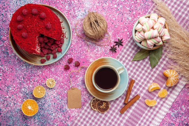 Draufsicht des roten Himbeerkuchens mit Zimt-Mandarinen und Tee auf der rosa Oberfläche