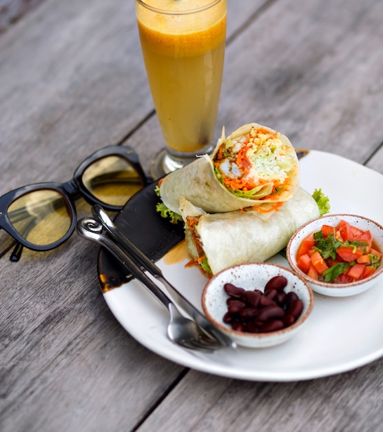 Draufsicht des roten Lippenstifts, des Essens und der lila Blume auf Holztisch. Foto der großen Platte mit leckerem Salat und Bohnen, die neben Glas Smoothie stehen.