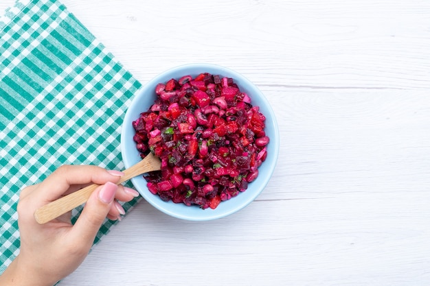 Draufsicht des Rübensalats, der mit Grüns innerhalb des blauen Tellers auf hellem Schreibtisch, Gemüsesalat des Gemüsehitamin-Lebensmittelmahlzeit geschnitten wird