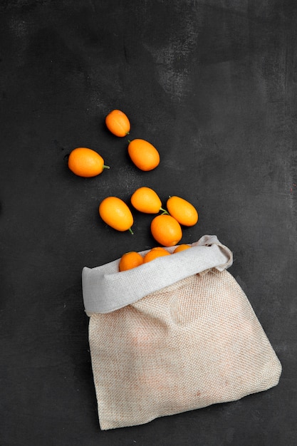 Kostenloses Foto draufsicht des sacks voller kumquats auf schwarzer oberfläche