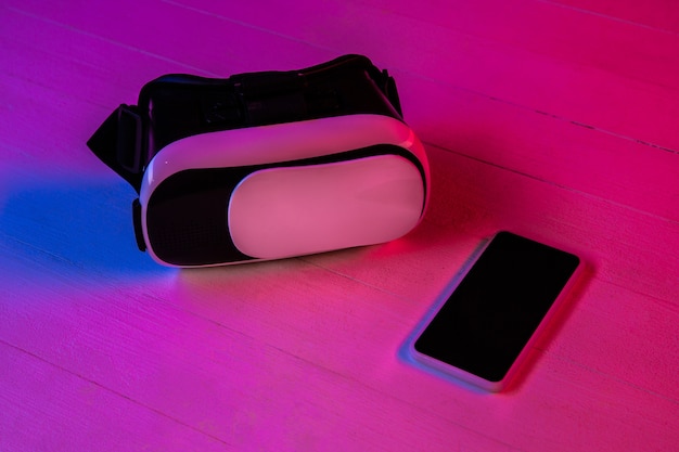 Draufsicht des Satzes von Gadgets in lila Neonlicht und rosa Hintergrund. Smartphone und VR-Headset. Copyspace für Ihre Werbung. Tech, modern, Gadgets. Virtuelle Realität.