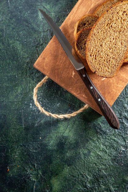 Draufsicht des Schwarzbrotmessers auf braunem Holzschneidebrett auf dunkler Oberfläche