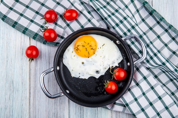 Draufsicht des Spiegeleis mit Tomaten in der Pfanne und auf kariertem Stoff auf Holz