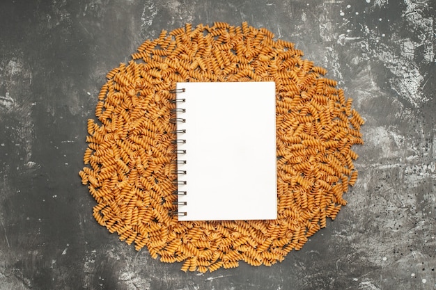 Draufsicht des spiralnotizbuchs auf roher italienischer pasta, die in einem kreis auf grauem hintergrund aufgereiht ist Kostenlose Fotos