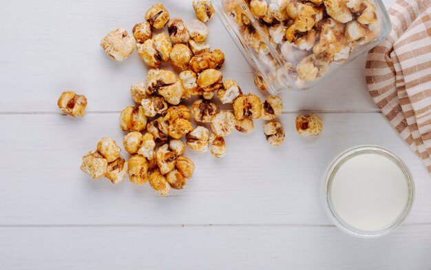 Draufsicht des süßen Karamellpopcorns verstreut vom Glas auf weißem Holztisch