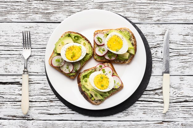 Draufsicht des Tellers mit Ei und Avocado-Sandwiches und Besteck