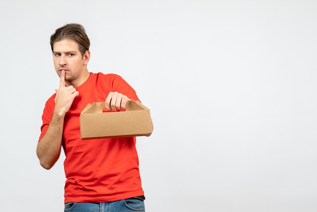 Draufsicht des überraschten und emotionalen jungen Mannes in der roten Bluse, die Kasten in den tiefen Gedanken auf weißer Wand hält