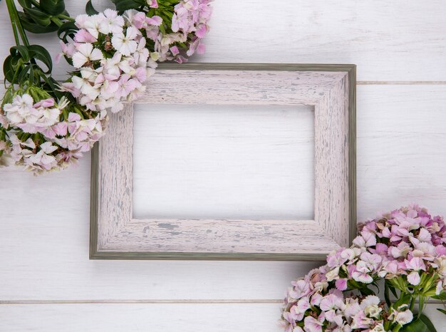 Draufsicht des weißen Rahmens mit Blumen auf einer weißen Oberfläche