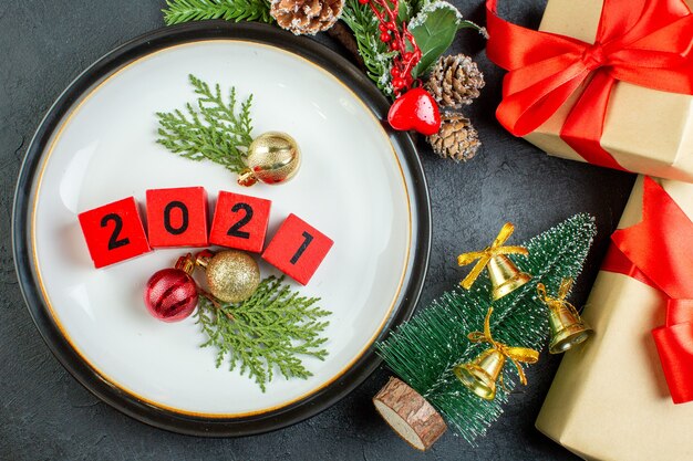 Draufsicht des Zahlendekorationszubehörs auf einem Plattentannenzweig-Nadelbaumkegel neben Weihnachtsbaum auf dunklem Hintergrund