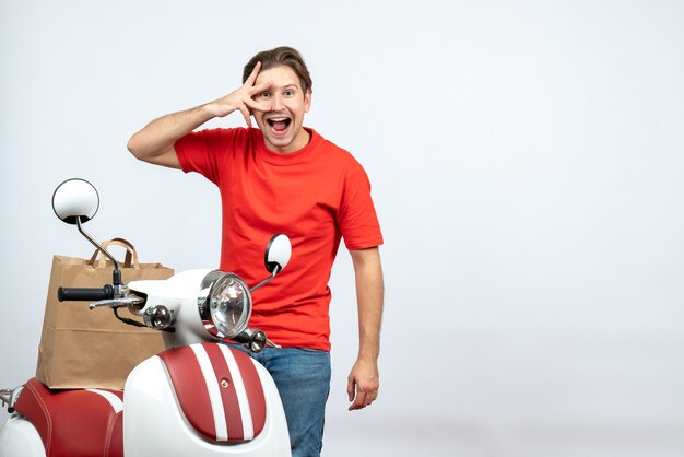 Draufsicht des zuversichtlichen Auslieferungsmannes in der roten Uniform, die nahe Roller hält Ordnung auf weißem Hintergrund steht